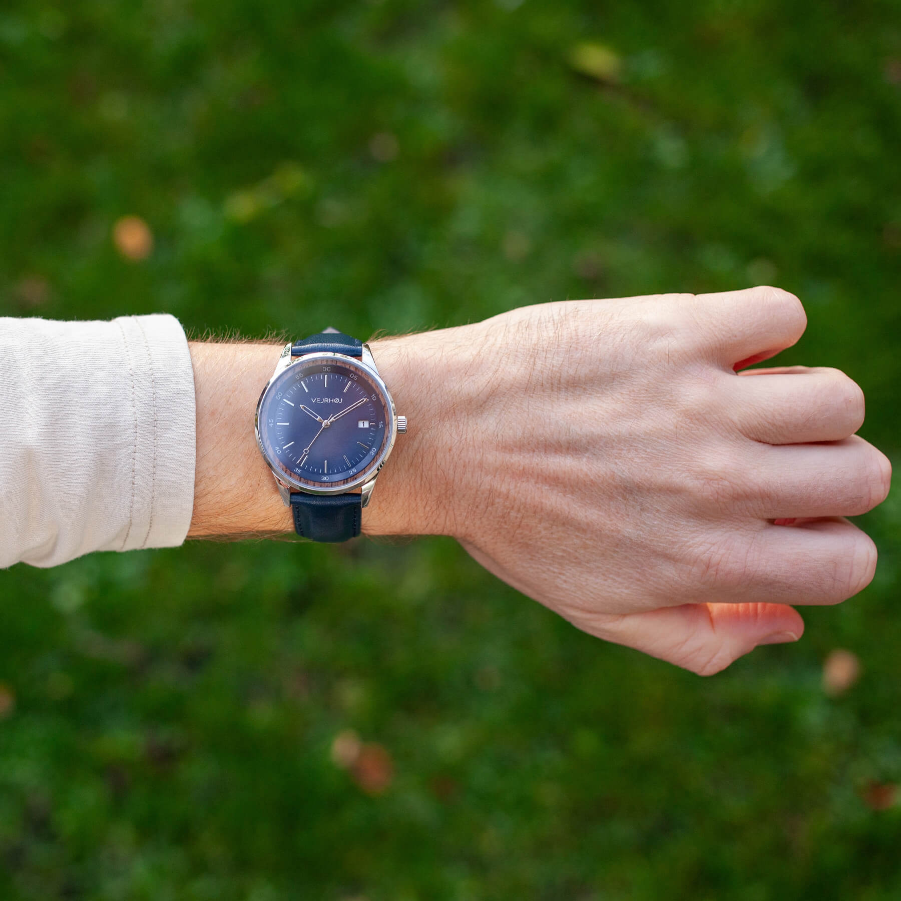 VEJRHØJ automatic blue watch on man's wrist with a green lawn in the background