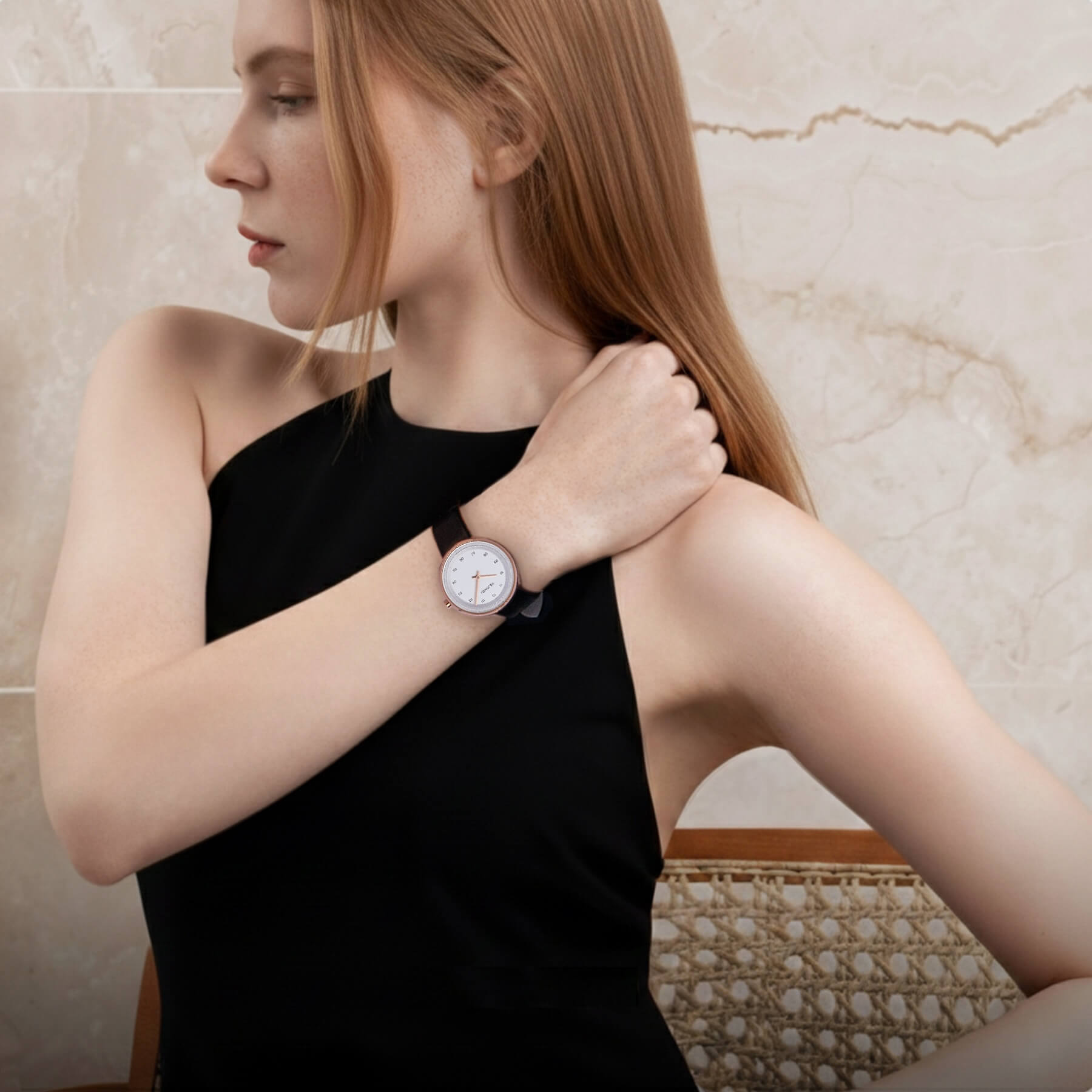 red haird woman wearing a black dress and a white VEJRHØJ watch with a marble background, sitting in a danish modern chair 