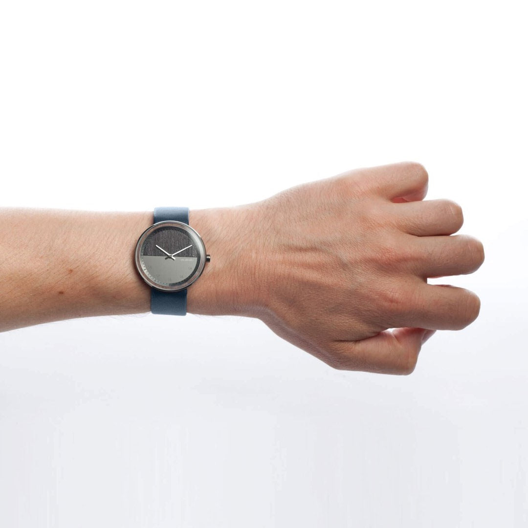 person wearing a dark wooden wrist watch with a two part steel and wood dial with blue straps
