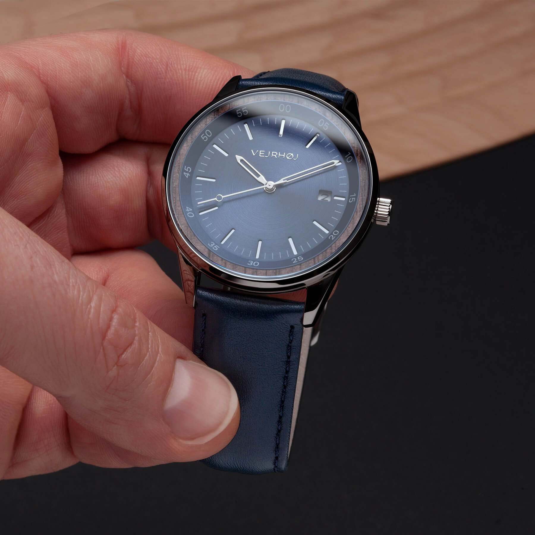 A blue automatic watch with silver hands and blue straps held by a hand