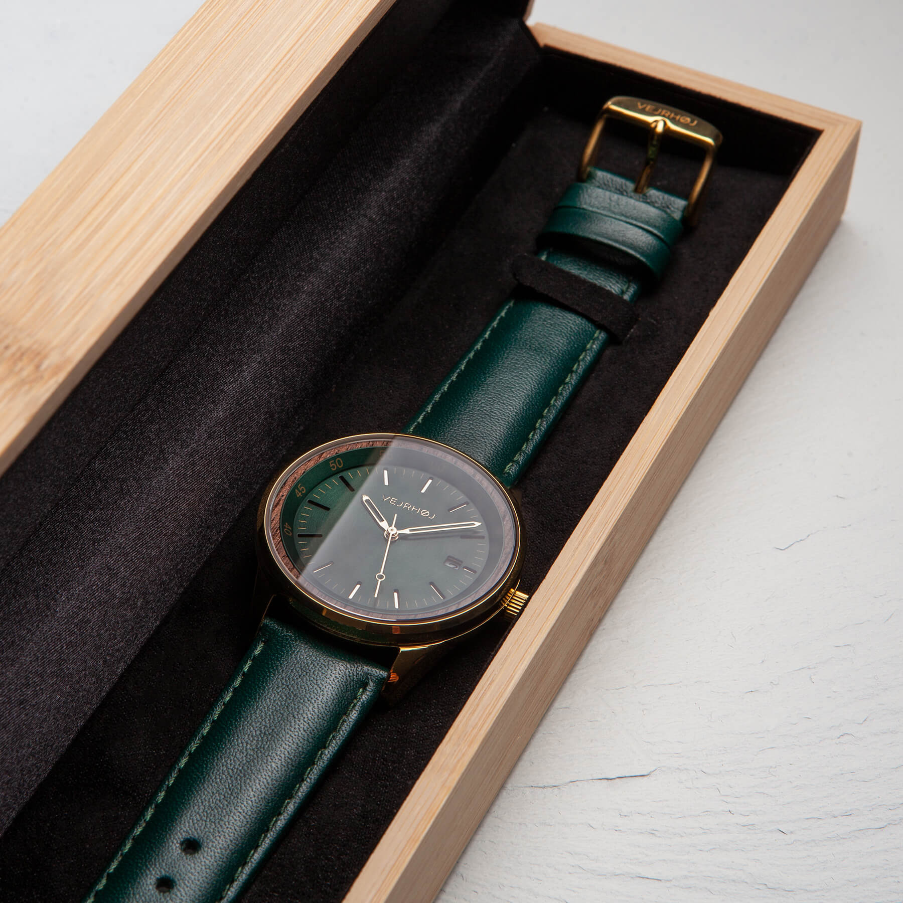 green automatic wrist watch with golden casing and green straps sitting inside the standard VEJRHOJ wooden box