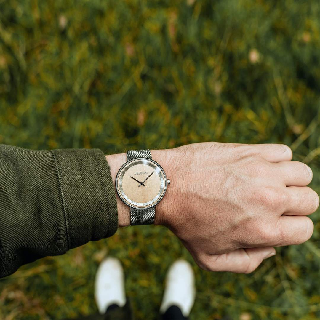 Person wearing a simple wooden watch with steel casing on top of grass